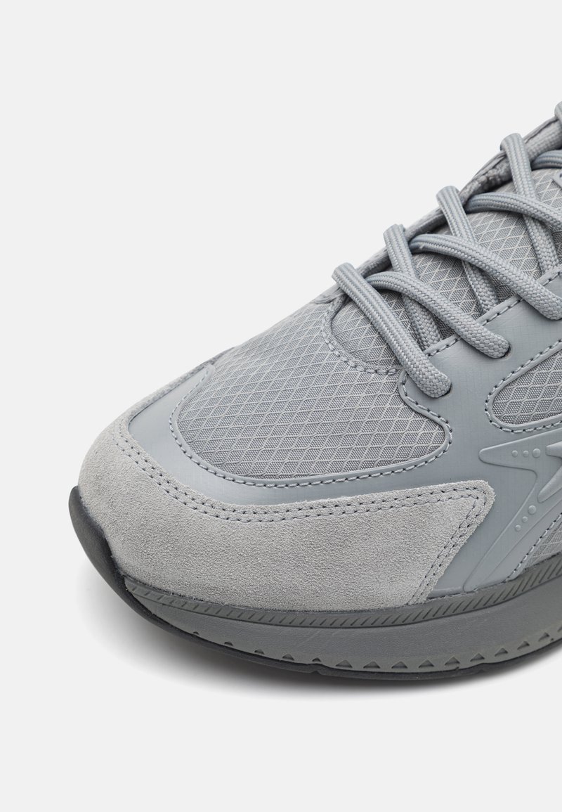 Szare buty sportowe z połączeniem materiałów siateczkowych i zamszowych, teksturowana powierzchnia, zaokrąglony czubek i płaska gumowa podeszwa.