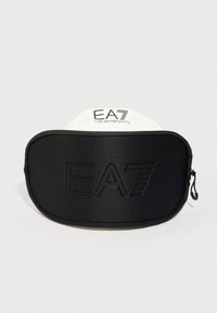 Černá pouzdro na zip s raženým logem EA7 a bílou visačkou nesoucí značku EA7 Emporio Armani na jednobarevném pozadí.