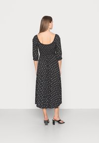 Vestido preto floral com mangas bufantes três quartos e costas baixas, apresentando um corte fluido a meio comprimento e padrões discretos de flores brancas.