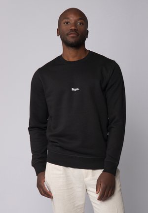 Black sweatshirt made of soft fabric, featuring a round neckline and ribbed cuffs. "Nope." is printed in white on the front.