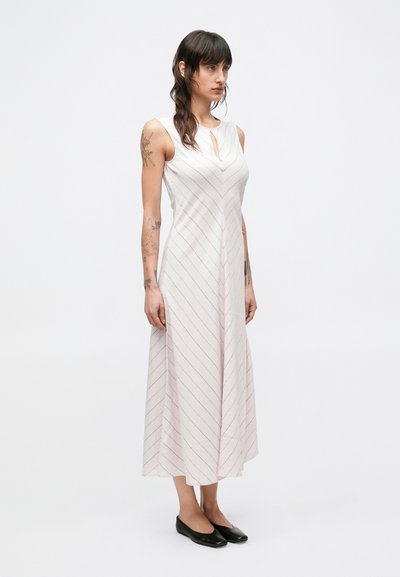 Biele šaty bez rukávov s ružovými diagonálnymi pruhmi, výstrihom s otvorom na hrudi a splývavou sukňou, v kombinácii s čiernymi balerínkami.