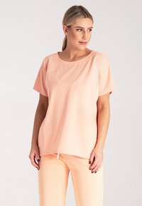 Koszulka w kolorze brzoskwiniowym z miękkiego materiału, z okrągłym dekoltem i krótkimi rękawami, o luźnym kroju i bezszwowym wykończeniu.