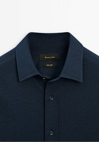 Chemise bleu marine à manches longues avec col pointu, boutonnée à l'avant, étiquette Massimo Dutti à l'intérieur du col.