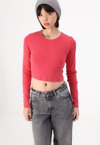 Sarkans ribots garām piedurknēm, īsā veidā, pieguļošs dizains, apvienots ar augsto jostasvietu pelēku džinsu. Modelis valkā pelēku bēniņu.