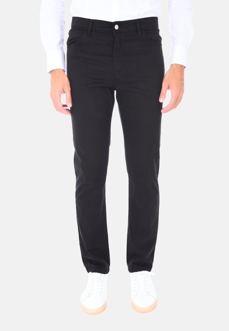 Pantaloni in denim neri con una vestibilità slim, dotati di tasche anteriori, zip e cuciture a contrasto, indossati con sneaker bianche.