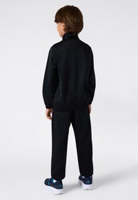 Czarny sportowy dres z kołnierzem stojącym i elastycznymi mankietami, w połączeniu z granatowymi butami z niebieskimi akcentami. Prosty design, gładka tekstura.
