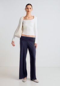 Balta garām piedurknēm topa un tumši zilu, plašu bikšu kombinācija. Apģērbā ir maiga, plūstoša vidukļa līnija un strukturēta bēša rokas soma.