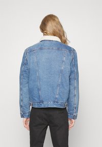 Light blue denim jack met een schapenvacht kraag, voorzien van contrasterende stiksels, knoopsluitingen en een getailleerde pasvorm. Achteraanzicht weergegeven.