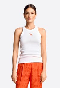 Weißes, geripptes Tanktop mit rundem Ausschnitt und rotem besticktem Logo, kombiniert mit strukturierten orangen Hosen.