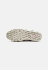 Sola de sapatilha Nike com um design texturizado em bege claro, apresentando o logo Swoosh em rosa e uma superfície de aderência padronizada para tração.