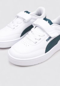 Baskets blanches avec une texture en cuir lisse, présentant une bande d'accent turquoise, un laçage à l'avant et une sangle Velcro pour un ajustement sécurisé.