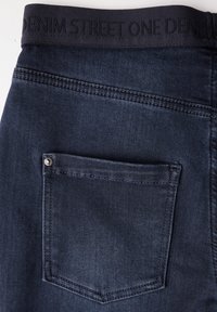 Mörkblå denimtyg med en synlig bakficka och sömnadsdetaljer. Den elastiska midjebandet har texten "DENIM STREET ONE" i svart.