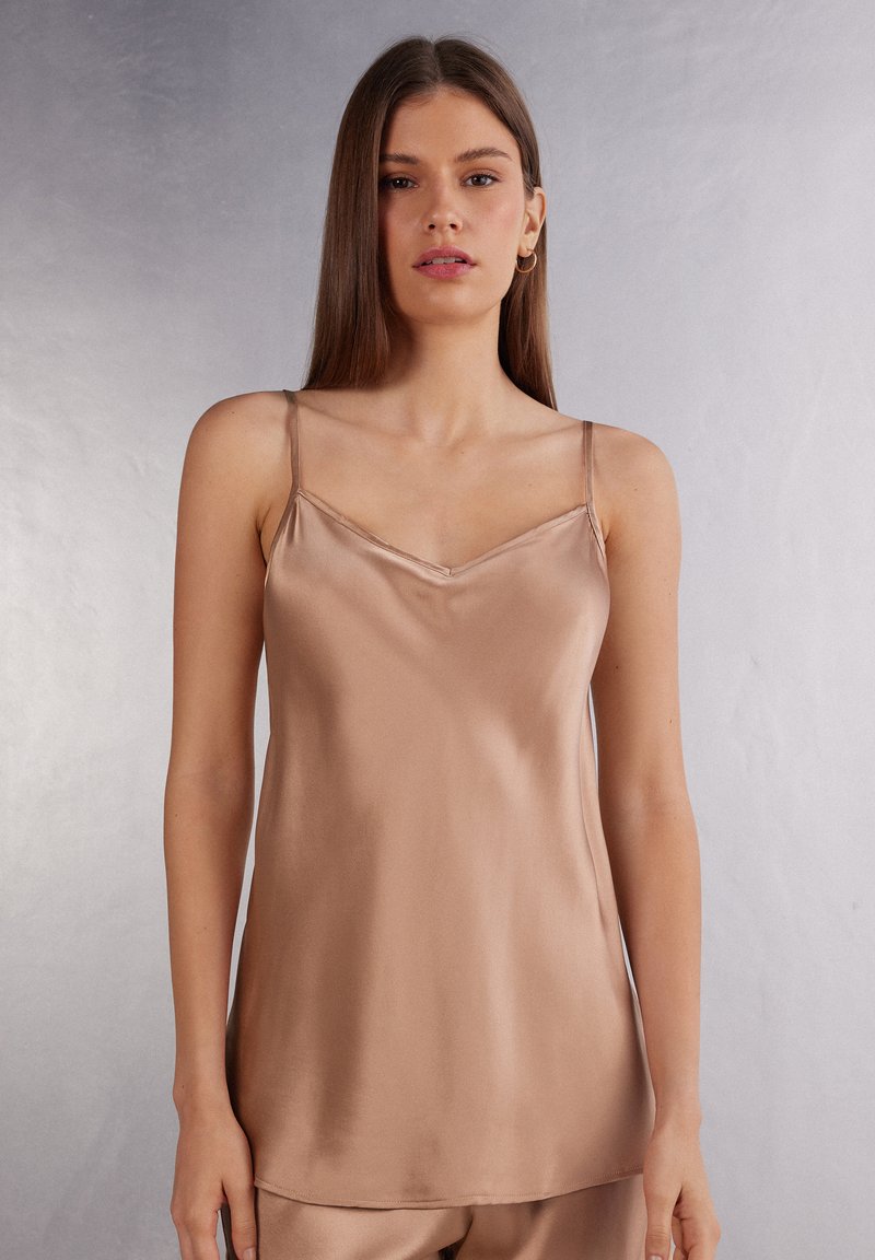 Camisola di raso marrone chiaro. Caratterizzata da spalline sottili e scollatura a V. Tessuto liscio con una vestibilità leggermente rilassata.