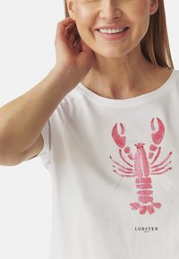 T-shirt blanc à manches courtes avec un motif graphique de homard rose centré sur la poitrine, accompagné du texte "LOBSTER LOCAL" en dessous.