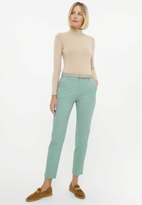 Miętowe dopasowane spodnie o prostym kroju, połączone z beżowym golfem i brązowymi zamszowymi loafersami. Wpleciony pasek z złotą klamrą.
