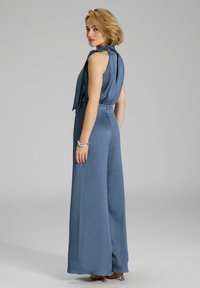 Blauwe jumpsuit met een mouwloos ontwerp, luxe stof, hoge hals en wijde broekspijpen. Beschikt over een opening aan de achterkant en een strikdetail bij de hals.