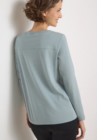 Light blue long-sleeve top with a rounded neckline, featuring a seam detail across the back and a relaxed fit, made from soft fabric.
