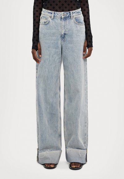Jeans de mezclilla de pierna ancha en un azul claro, con una cintura alta, dobladillo deshilachado y detalles de costura visibles.