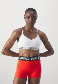 Fehér sportmelltartó fekete Nike logóval, piros, testhez simuló rövidnadrággal kombinálva, fekete elasztikus derékpánttal és Nike felirattal.