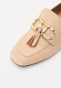 Beige läderloafers med fyrkantig tå, prydda med ett spänne i guldton och detalj med fransar. Slät textur med subtila sömdetaljer.
