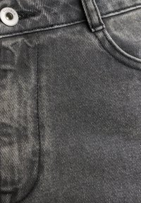 Ciemnoszara tkanina dżinsowa o lekko wyblakłej strukturze. Posiada metalowy guzik i przeszycia wzdłuż szwów, co podkreśla klasyczny fason dżinsów.