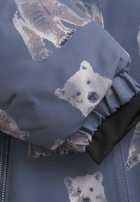 Lyseblå jakke lavet af stof med et gentaget print af isbjørne i nuancer af hvid og beige. Dæmpede ærmer med sorte elastiske detaljer.