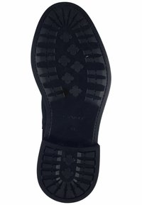La semelle en caoutchouc noir présente un motif de bande de roulement texturé avec des formes croisées en relief. Bords lisses avec un logo de marque en relief. Taille 41 visible.
