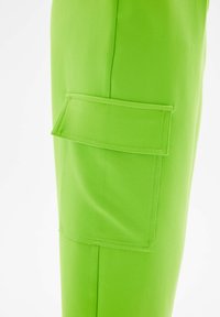 Groene broek van gladde stof met een grote patch-zak aan de zijkant. De kleur is helder, met subtiele stikseldetails.
