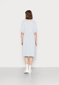 Vestido floral azul com mangas curtas em balão, cintura franzida e saia até ao joelho, combinado com botas brancas até aos tornozelos sobre uma superfície cinza-claro.