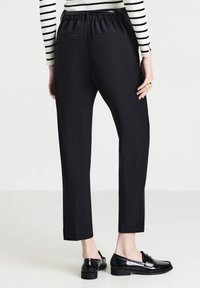 Pantalons noirs ajustés avec une taille élastique, deux poches arrière et des jambes droites. Portés avec des mocassins en cuir noir.
