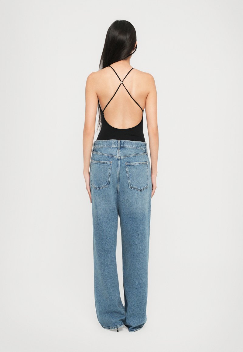 Un bodysuit noir avec un dos décolleté et des bretelles croisées associé à un jean en denim léger bleu clair, ample, avec deux poches arrière.