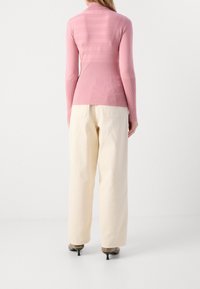 Long-sleeve, ribbed pink top with a high collar and striped texture at the back, paired with loose-fitting, cream-colored pants.
