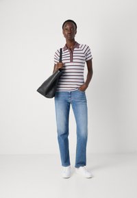 Striped polo shirt i hvit og burgunder, med krage og knappestolpe, kombinert med lyseblå jeans og hvite joggesko, bærende en svart veske.