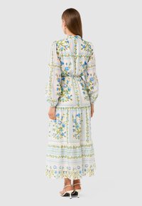 Floral-patterned maxi dress in light blue and white, with long puffed sleeves, fitted waist, and tiered skirt; features adjustable tie detail.