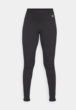 Fekete leggings rugalmas anyagból, magas derékkal és egy kis logó jelöléssel a bal csípőn. Sima textúra.