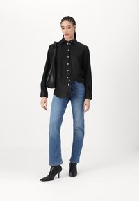 Camicia nera con bottoni e maniche lunghe, abbinata a jeans blue a gamba dritta e stivaletti neri a punta. Design semplice e minimalista.