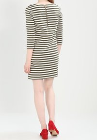 Pruhované šaty se zelenými a bílými horizontálními pruhy, kulatým výstřihem, tříčtvrtečními rukávy a zlatým zipem na zadní straně.