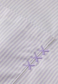 Tissu rayé violet clair et blanc présentant des lignes texturées, avec des accents brodés à la main visibles dans un violet assorti.