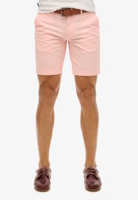 Pantalones cortos rosas de material ligero, de corte ajustado, con dobladillo rematado, combinados con zapatos de barco burdeos y un cinturón marrón.