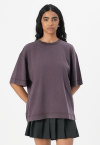 T-shirt oversized a maniche corte di colore viola, realizzato in cotone morbido. Presenta un collo rotondo e una vestibilità rilassata. Abbinato a una gonna plissettata.