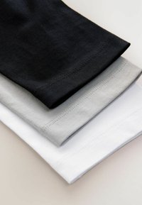 Tre pezzi di tessuto in cotone piegati e impilati, mostrando orli neri, grigi e bianchi con cuciture visibili.
