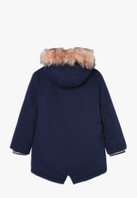 Parka de invierno azul marino con mangas largas y capucha, con un suave forro de piel sintética marrón claro, vista desde atrás sobre un fondo blanco.