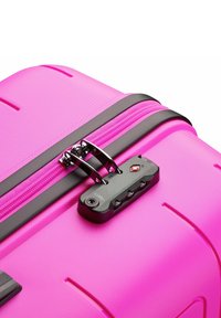 Valigia rigida rosa con superficie testurizzata, zip nera e lucchetto a combinazione integrato. Presenta bordi arrotondati e design aerodinamico.