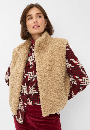 Vriendelijke beige mouwloze vest met een hoge kraag, gecombineerd met een rode en gemusterde lange mouwen shirt en bordeauxrode broek. Zachte textuur overal.