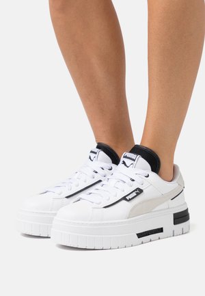 Zapatillas deportivas blancas de plataforma hechas de cuero con acentos en negro y beige. Cuentan con una suela de goma gruesa y un diseño de cordones con la marca en la lengüeta.