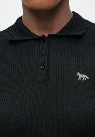 Melnā ribota polo krekla ar apkakles kaklu, trim melniem pogām un nelielu pelēku lapsas logotipu kreisajā krūtī.