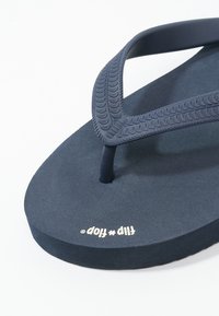 Tumed rinnaga flip-flop, millel on tekstuuriga rihm ja pehme vahtpõhi. Omab minimalistlikku disaini ja trükitud logo jalaaluses.