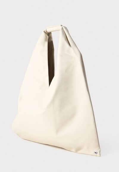 Bolsa de tote em pele bege com um design único e descontraído, apresentando uma alça retangular e um detalhe de fecho com botão de pressão.