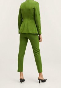 Blazer verde ajustado con hombros estructurados y dobladillo acampanado, combinado con pantalones verdes de corte slim y tacones negros finos.