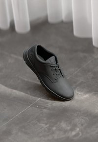 Zapatos de cuero negro con una textura suave, punta redonda y diseño de cordones. Detalle sutil del logo en el lateral y suela de goma.